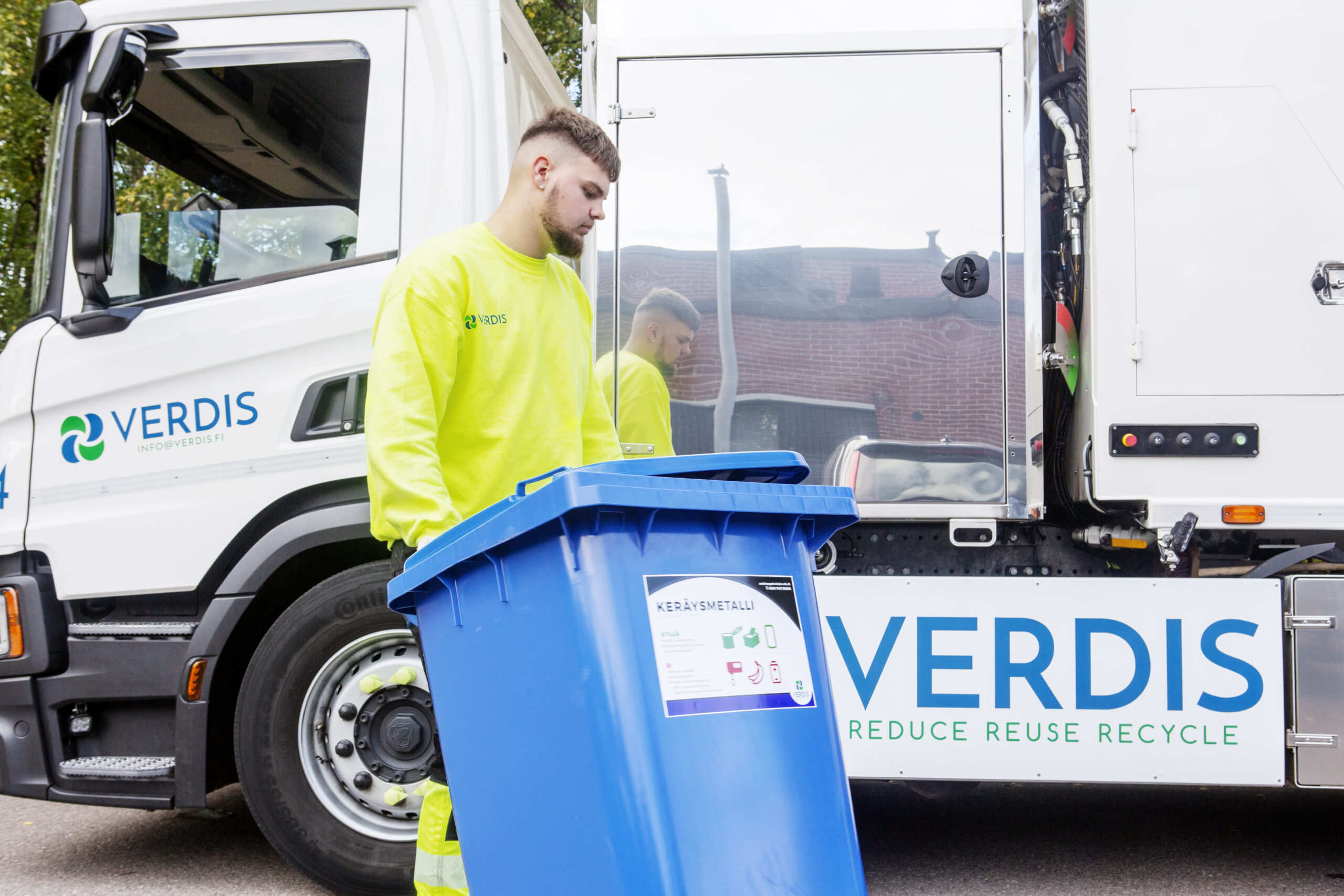 Kuljettaja sinisen jäteastian kanssa Verdiksen jäteauton edessä.